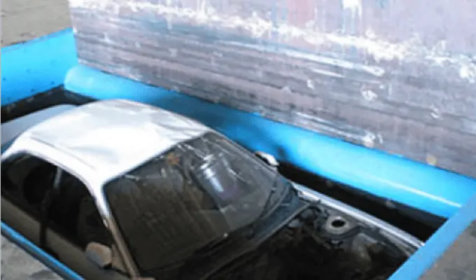 廃車処理用の油圧プレス機で自動車の上部が押し潰されている様子