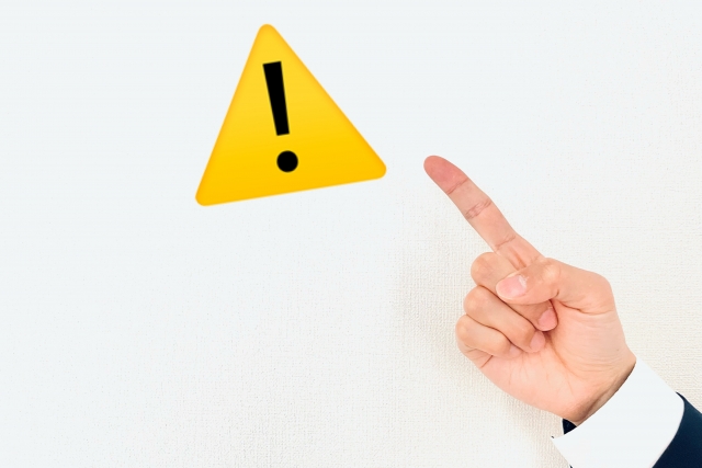 注意マークを指さす手元