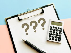 ハテナが描かれた紙と電卓とボールペン